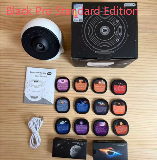 Galaxy Star Projector Light — flat lay of Black Pro Standard Edition showing white projector, product box, user manual, 12 film discs, USB cable, and accessory boxes on a wooden surface