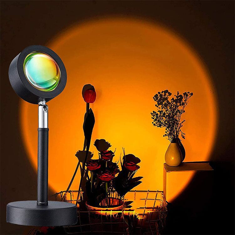 Sunset Projection Lamp — RGB App-Controlled Ambient Light — sunset lamp projecting a warm orange glow on a wall beside a vase with dried plants